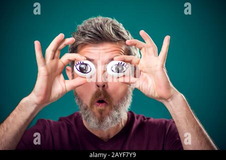 Ein Porträt eines lustigen bärtigen Mannes in rotem T-Shirt, das Eier hinter Augen hält. Menschen, Emotionen und Essenskonzept Stockfoto