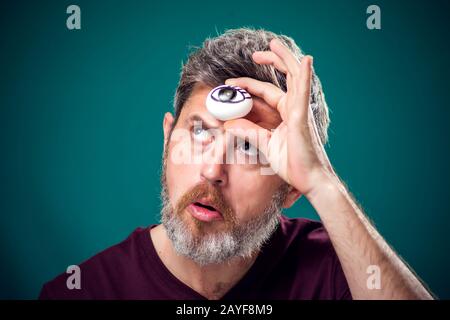 Ein Porträt des bärtigen Mannes in rotem T-Shirt, das Ei mit dem Zeichenauge hinter der Stirn als drittes Augensymbol hält. Stockfoto