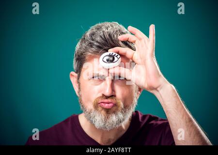 Ein Porträt des bärtigen Mannes in rotem T-Shirt, das Ei mit dem Zeichenauge hinter der Stirn als drittes Augensymbol hält. Stockfoto