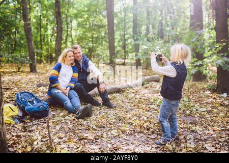 Reise, Tourismus, Wanderung, Technik und Familienkonzept. Glückliches Kind macht Foto-Eltern in Wald. Mutter und Papa posieren für Foto, doen Stockfoto