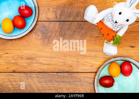 Sechs bunte Ostereier auf zwei Tellern und Osterhase mit Holzhintergrund Stockfoto