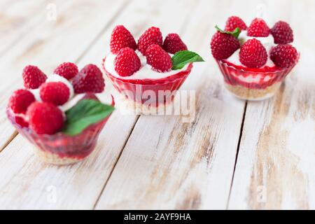 Trifle mit Himbeeren, Minze und Käsekuchen auf altem weißen Holzhintergrund. Traditionelles süßes Dessert in englischer Sprache. Stockfoto