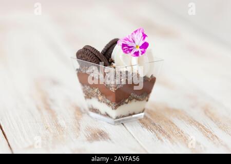 Schwarz-weiße Schokolade mit Plätzchen triflen. Dekoriert mit einer Blume auf altem weißen Holzhintergrund. Traditionelles süßes Dessert in englischer Sprache. Stockfoto