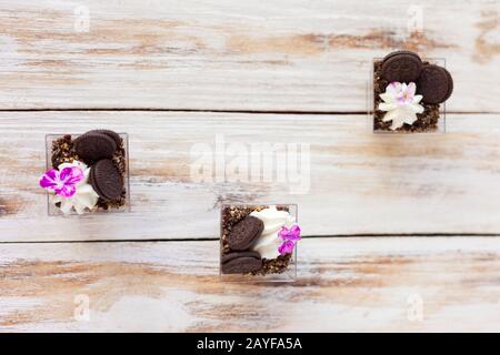 Schwarz-weiße Schokolade mit Plätzchen triflen. Dekoriert mit einer Blume auf altem weißen Holzhintergrund. Traditionelles süßes Dessert in englischer Sprache. Stockfoto