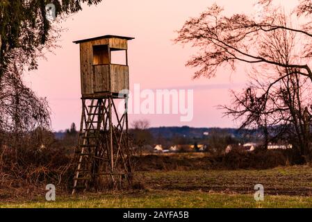 Jagdturm nach Sonnenuntergang in ländlicher Landschaft gegen rosafarbenen Himmel. Rehe stehen in der Nähe von Zettling Graz in Österreich. Stockfoto