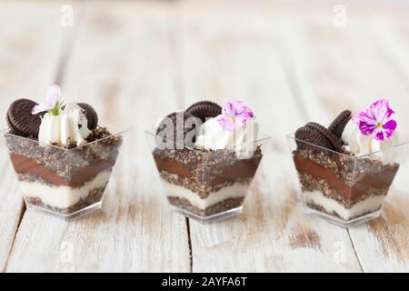 Schwarz-weiße Schokolade mit Plätzchen triflen. Dekoriert mit einer Blume auf altem weißen Holzhintergrund. Traditionelles süßes Dessert in englischer Sprache. Stockfoto