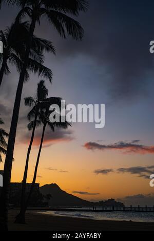 Sunrise Skies Hinter Diamond Head auf der Insel Oahu vom Waikiki Beach Mit Palmen im Vordergrund Stockfoto