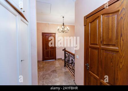 Treppe im Cottage. Marmorstufen, schmiedeeisernes Geländer, Holzhandläufe. Schmiedeeiserner Kronleuchter. Holztür auf der Landung. Stockfoto