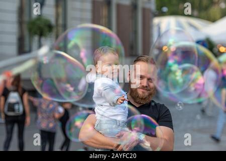 Altstädter Ring, Riga, Lettland - 16. August 2019: Bärtiger Mann mit einem Kind an den Händen wacht und freut sich über die gigantischen Seifenblasen Stockfoto