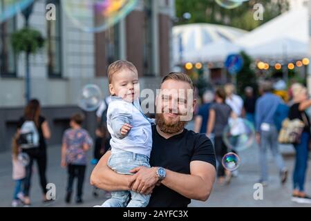 Altstädter Ring, Riga, Lettland - 16. August 2019: Bärtiger Mann mit einem Kind an den Händen wacht und freut sich über die gigantischen Seifenblasen Stockfoto