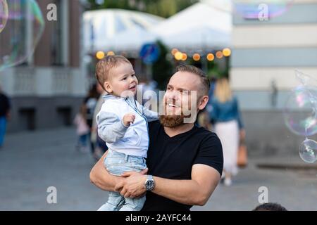 Altstädter Ring, Riga, Lettland - 16. August 2019: Bärtiger Mann mit einem Kind an den Händen wacht und freut sich über die gigantischen Seifenblasen Stockfoto