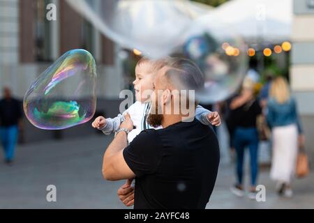 Altstädter Ring, Riga, Lettland - 16. August 2019: Bärtiger Mann mit einem Kind an den Händen wacht und freut sich über die gigantischen Seifenblasen Stockfoto