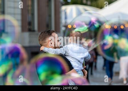 Altstädter Ring, Riga, Lettland - 16. August 2019: Bärtiger Mann mit einem Kind an den Händen wacht und freut sich über die gigantischen Seifenblasen Stockfoto