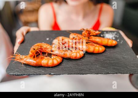 Glückliche Asianerin im Hut, die lokale spanische Küche mit gegrillten Meeresfrüchten isst Stockfoto