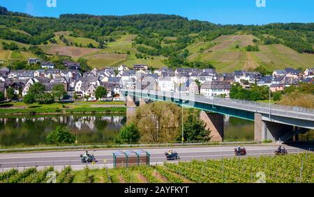 Brücke über die hier gelegene Mosel, die zum Dorf Wolf und den umliegenden Weinbergen führt, auf den Hügeln unter blauem Himmel. Wolf, Trabentrarbach, Deutschland. Stockfoto
