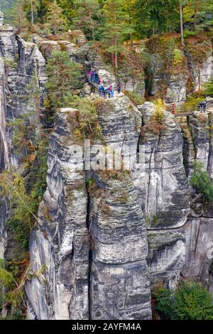 Touristen an einem Aussichtspunkt auf einer steilen Klippe mit Blick über die Felsformation Bastei, einem Teil des Elbsandsteingebirges. Sachsen, Deutschland. Stockfoto