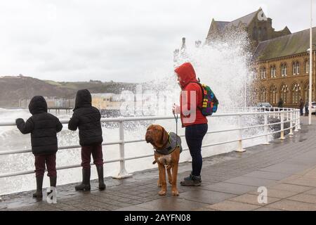 Aberystwyth, Ceredigion, Wales, Großbritannien. Februar 2020. Wetter in Großbritannien: Eine Frau und zwei Kinder beobachten die Wellen, während die Meeresschutzgebiete entlang der Küstenstadt Aberystwyth eine weitere Schande Unternehmen, als Storm Dennis das Meer hochkreist und dabei riesige abstürmende Wellen entlang der Promenade erzeugt. Kredit: Ian Jones/Alamy Live News Stockfoto