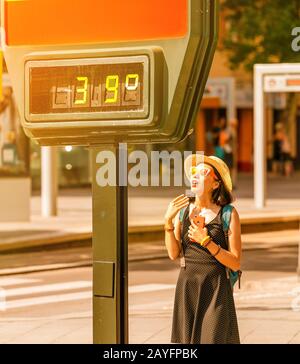 Frau leidet bei heißem Wetter im Freien unter Hitze und Sonneneinschlag vor dem Hintergrund eines Straßenthermometers mit 39 Grad Celsius Stockfoto