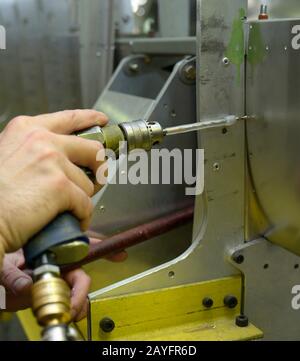 Montiertere Hände, die mit einem pneumatischen Bohrer mit Pistole arbeiten, bereiten den Teil der Karosserieebene für das weitere Nieten vor Stockfoto