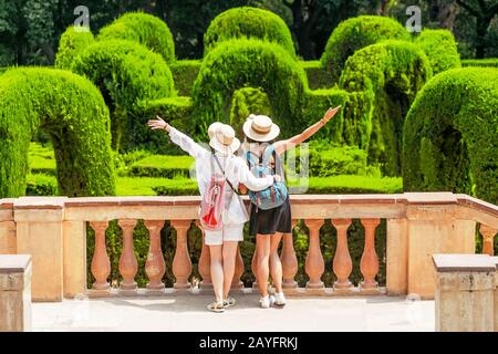 Zwei glückliche Freundinnen, die gemeinsam im Parklabyrinth in Barcelona spazieren gehen Stockfoto