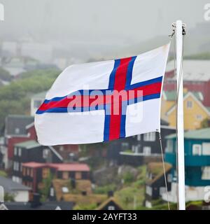 Flagge des Faeroeers vor Häusern in Nebel, auf den Färöern, in Streymoy, in Torshavn Stockfoto