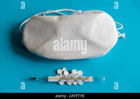 Thermometer, Pillen und eine Schutzmaske auf blauem Hintergrund. Virenschutz- und Behandlungskonzept. Stockfoto