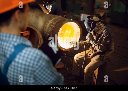 Schweißer arbeitet im Werk, Arbeiter im Hintergrund Stockfoto