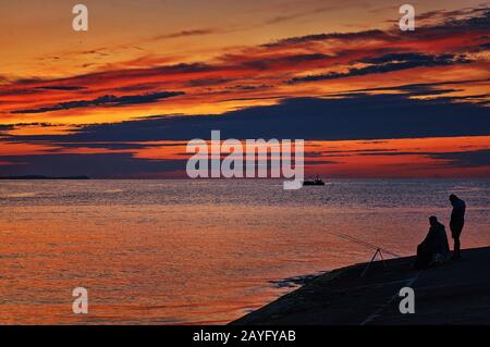 Angler am Ostseedamm bei Sonnenuntergang. Stockfoto