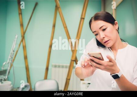 Beratung für ein geeignetes Medikament. Schöne junge Afrikanerin im Labormantel, die Behälter mit etwas Arznei hält und auf dem Handy telefoniert, während sie steht Stockfoto