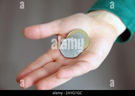 Ein kleiner Junge hält 2,50 £in der Hand mit einem Kew Gärten 50p im Wechsel und einer 2 £Münze Stockfoto