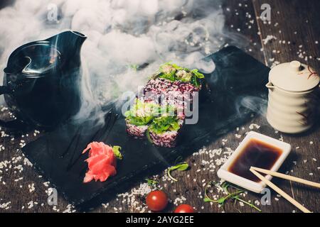 Verschiedene Sushi auf weißem Teller mit Essstäbchen auf Holzhintergrund Stockfoto