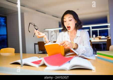 Überraschte Frau liest Buch in Bibliothek Stockfoto