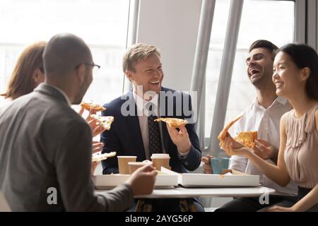 Fröhliche Kollegen aus mehreren ethnischen Gruppen unterhalten sich mit Pizza im Büro Stockfoto