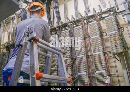 Der Mann verlegt das Kabel im Serverraum des Rechenzentrums. Der auf der Treppe stehende Ingenieur arbeitet mit der Schalteinrichtung des Teleps Stockfoto