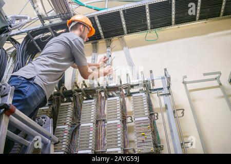 Der auf der Treppe stehende Ingenieur arbeitet mit der Schalteinrichtung der Telefonbörse. Der Mann verlegt das Kabel in den Serverraum von Th Stockfoto