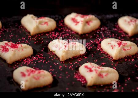 Herzförmige Butter spritzt Plätzchen mit rotem Zucker streut den Fokus auf Herzbokeh Stockfoto