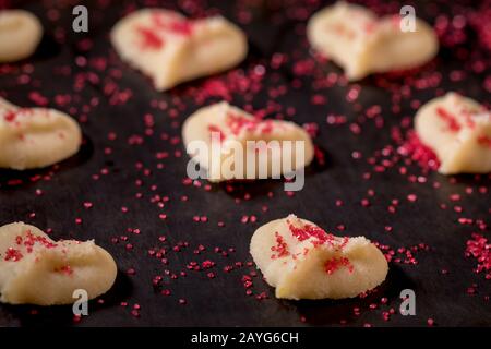 Herzförmige Butter spritzt Plätzchen mit rotem Zucker streut den Fokus auf Herzbokeh Stockfoto