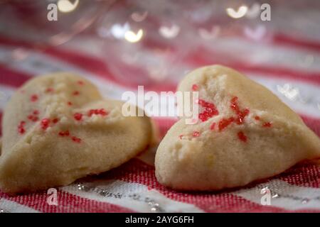 Herzförmige Butter spritzt Plätzchen mit rotem Zucker streut den Fokus auf Herzbokeh Stockfoto