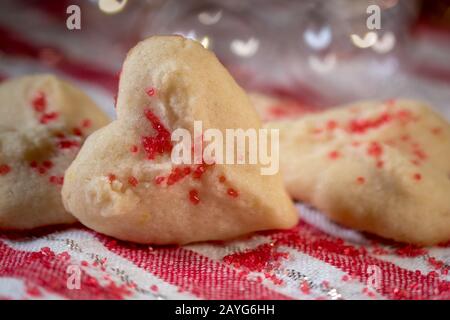 Herzförmige Butter spritzt Plätzchen mit rotem Zucker streut den Fokus auf Herzbokeh Stockfoto