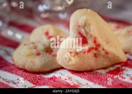 Herzförmige Butter spritzt Plätzchen mit rotem Zucker streut den Fokus auf Herzbokeh Stockfoto