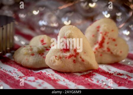 Herzförmige Butter spritzt Plätzchen mit rotem Zucker streut den Fokus auf Herzbokeh Stockfoto