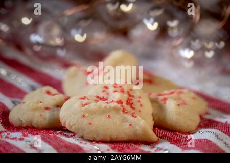 Herzförmige Butter spritzt Plätzchen mit rotem Zucker streut den Fokus auf Herzbokeh Stockfoto