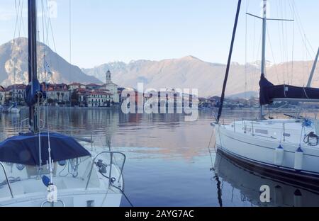 Der Lago Maggiore, Segelboote, die in einem kleinen Hafen vor einem malerischen Dorf festgemacht wurden Stockfoto