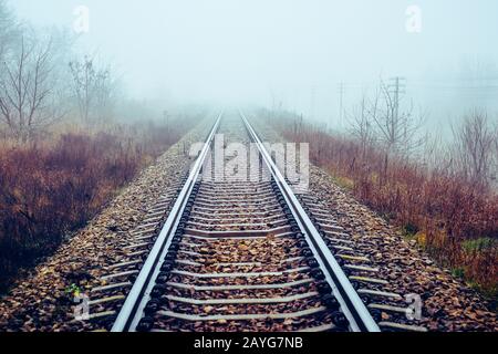 Die Perspektive der Bahngleise verschwindet morgens in Nebel Stockfoto