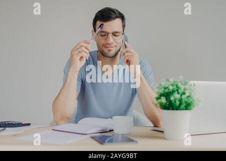 Ein vielbeschäftigter Mann arbeitet an organisatorischen Problemen, spricht mit dem Geschäftspartner per Handy, hält die Augen geschlossen, während er versucht, sich an die notwendigen Informationen zu erinnern Stockfoto