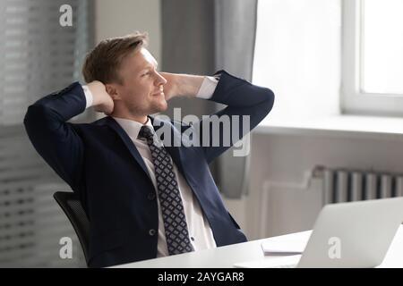 Nachdenklicher männlicher Mitarbeiter entspannt sich im Sessel, der am Arbeitsplatz träumt Stockfoto