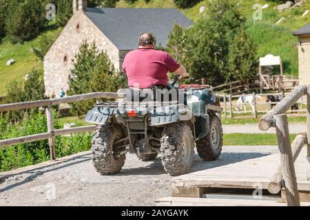 24. JULI 2018, NURIA, SPANIEN: Fat Man on the Quad Bike in Mountain Village Stockfoto
