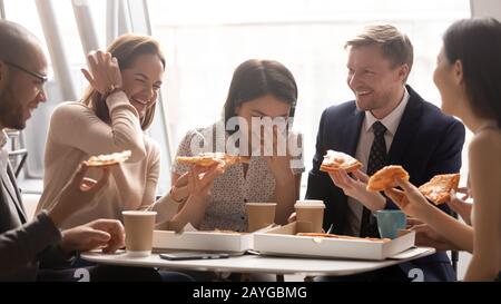 Lächelnde Mitarbeiter lachen darüber, gemeinsam Pizza im Büro zu haben Stockfoto