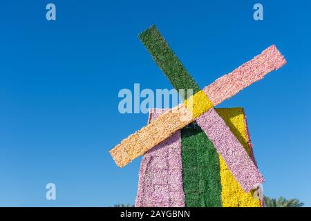 Eine in Rosa, Grün und Gelb gefärbte Blumenwindmühle an einem sonnigen Tag am blauen Himmel bei einer Feier im Freien. Niederländisches oder niederländisches Thema oder Konzept. Stockfoto