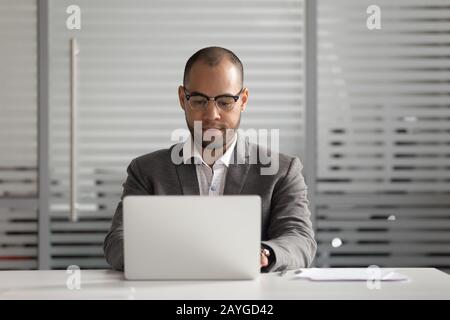 Konzentrierter Geschäftsmann in Brille, der mit der Arbeit am Laptop beschäftigt ist Stockfoto